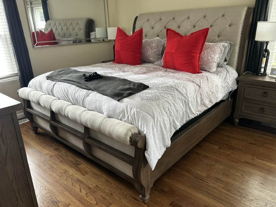 Neatly made bed with tufted headboard, red accent pillows, and hardwood floor