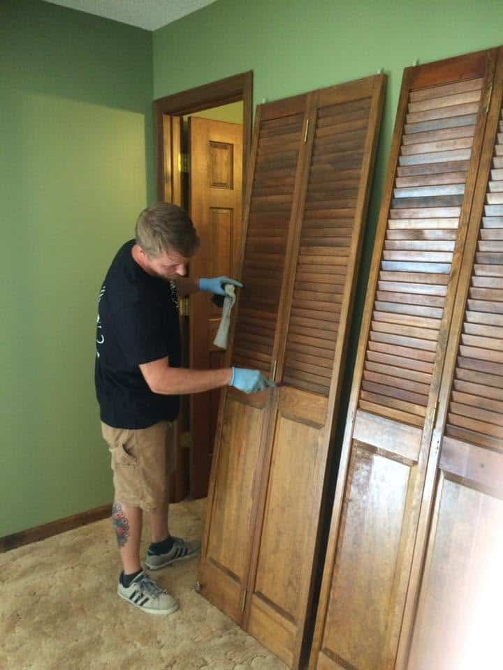 Cleaner in gloves wiping louvered wood closet doors in an empty room